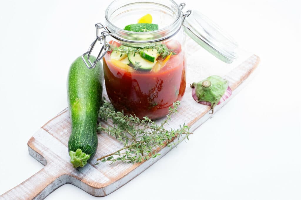 Tomatensuppe mit Zucchini im Einmachglas auf Holzbrett mit Thymian und ganzer Zucchini